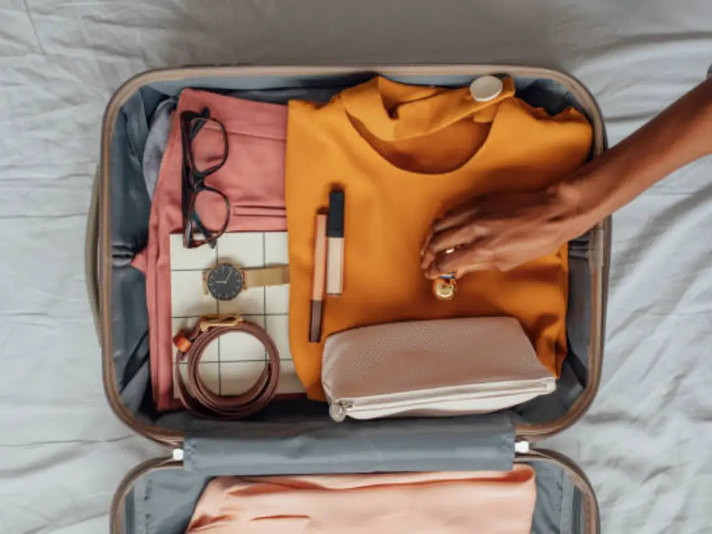 A person packing a small travel-size perfume bottle into a suitcase