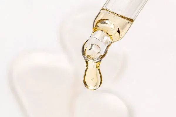 Close up macro photography of a glass pipette dispensing a single drop of serum