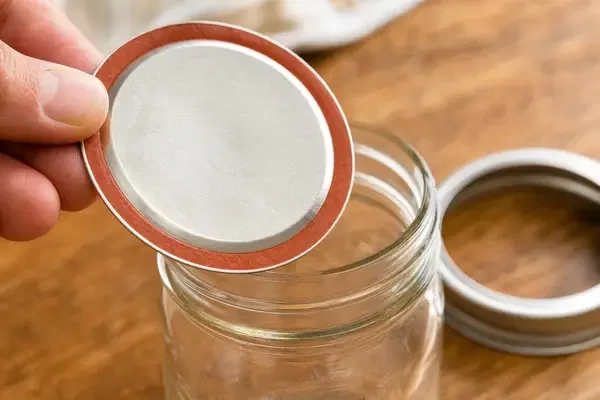 Close-up of a two-piece Mason jar lid being applied, highlighting the threaded band and flat sealing lid