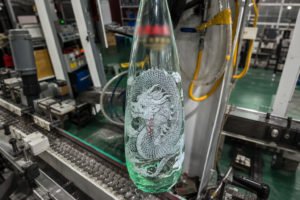 Multi-color screen printed dragon artwork on a clear glass bottle on the production line
